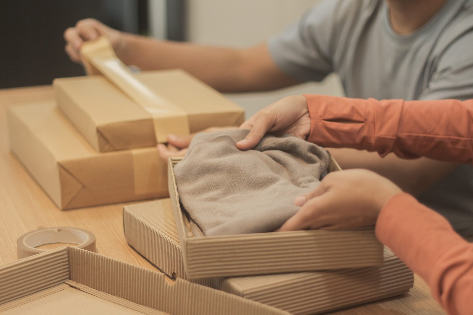 Two people putting clothes inside boxes and wrapping them